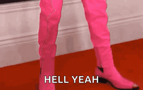 a person wearing pink cowboy boots is standing on a red carpet and says `` hell yeah '' .
