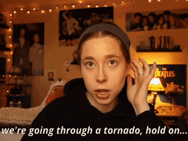 a woman covering her ear with her hand with the words we 're going through a tornado hold on behind her