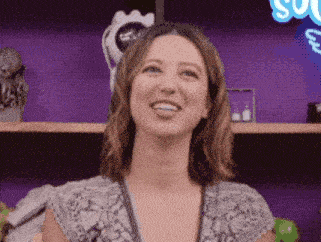 a woman is making a funny face in front of a purple shelf .