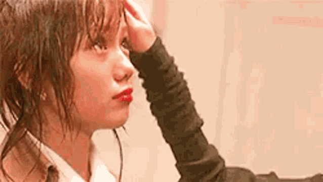 a woman is holding her hand to her forehead while looking at herself in the mirror .