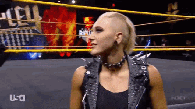 a woman is standing in a wrestling ring wearing a black leather vest .