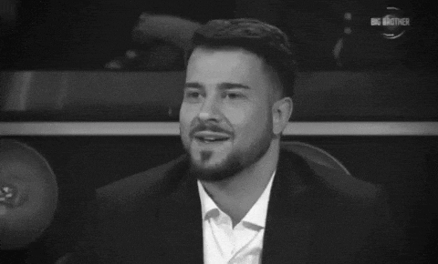 a man with a beard is smiling in a black and white photo with the big brother logo in the background