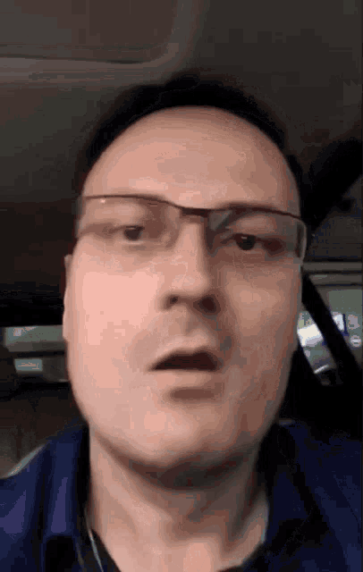 a man wearing glasses and a blue shirt makes a surprised face