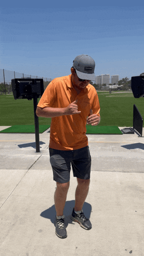 a man wearing an orange shirt and gray shorts is standing in front of a golf course