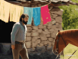 a man standing next to a horse in front of a stone wall with clothes hanging from it