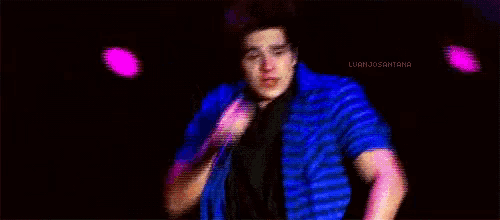 a man in a blue plaid shirt sings into a microphone in front of flames