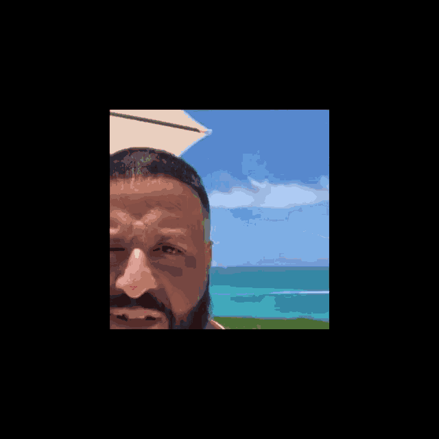 a man with a beard is standing in front of a beach and looking at the ocean .