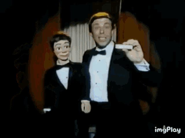 a man in a tuxedo is standing next to a puppet .