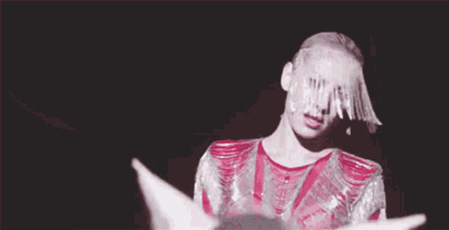 a woman in a red and silver dress with a veil on her face is standing in a dark room .