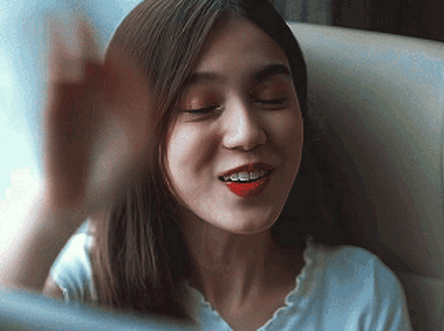 a woman with red lipstick and braces on her teeth is smiling and waving her hand .