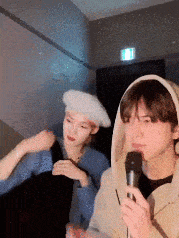 a man in a hooded sweatshirt is holding a microphone next to a woman in a beret .