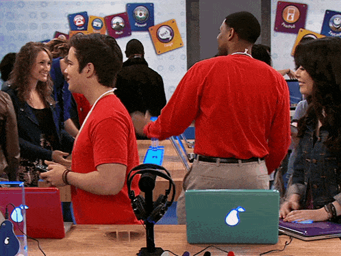 a man in a red shirt is talking to a woman in front of a wall with stickers on it