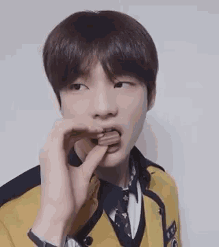 a young man in a school uniform is eating a chocolate bar with his hand .