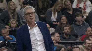 a man in a blue suit and white shirt stands in front of a crowd of people