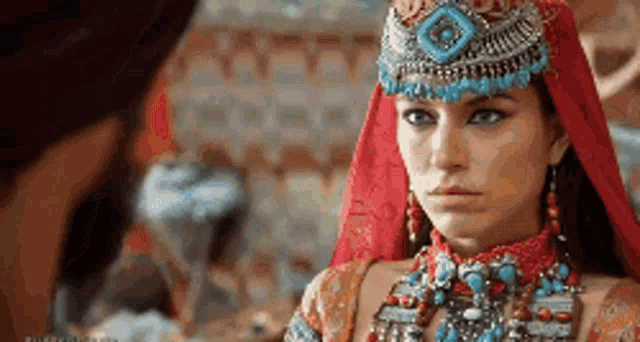 a woman in a red and blue costume is wearing a necklace and a headpiece .