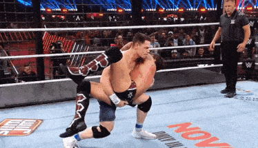 two men are wrestling in a wrestling ring with the word now on the ground