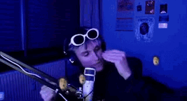 a man wearing headphones and goggles is sitting in front of a microphone .