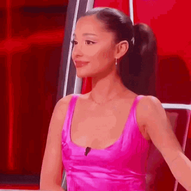 ariana grande is wearing a pink dress and ponytail while sitting in a chair .