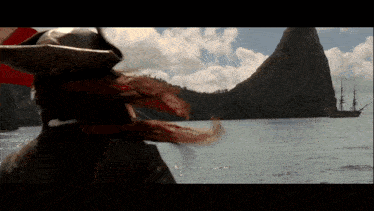 a man in a pirate hat and scarf stands in front of a body of water