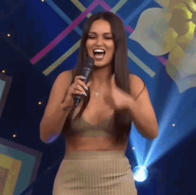 a woman is singing into a microphone on a stage while wearing a crop top and skirt .