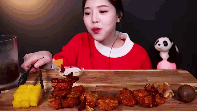 a woman in a red sweater is eating chicken on a wooden cutting board