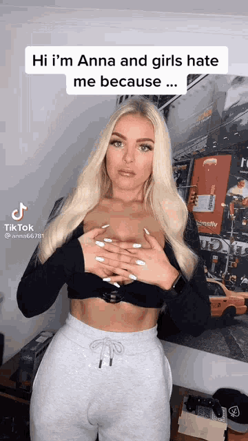 a woman is wearing a black crop top and grey sweatpants and holding her breasts .