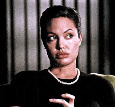 a woman is wearing a pearl necklace and a black shirt .