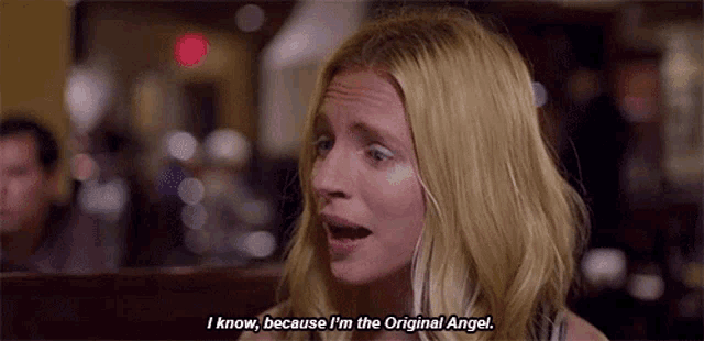 a woman is sitting at a table in a restaurant and saying i know , because i 'm the original angel .