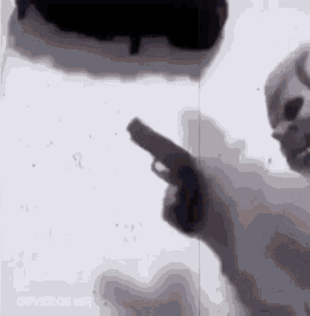 a person is holding a gun in their hand in front of a white wall .