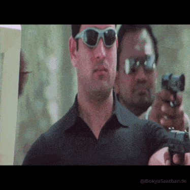 a man wearing sunglasses is pointing a gun at the camera