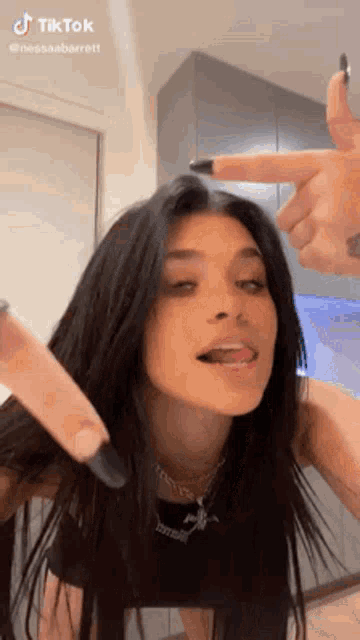 a woman with long black hair is making a funny face with her tongue out and pointing at her hair .