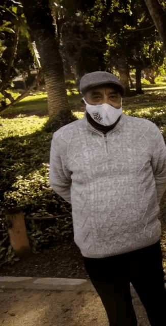 a man wearing a face mask stands in a park with trees in the background