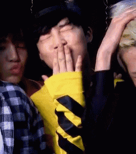 a man in a yellow jacket is covering his mouth with his hands while another man looks on .