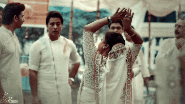 a woman in a white dress is dancing in front of a group of people and the word creations is on the bottom left