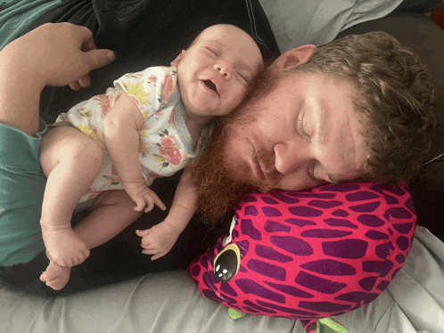 a man laying on a bed with a baby and a purple pillow