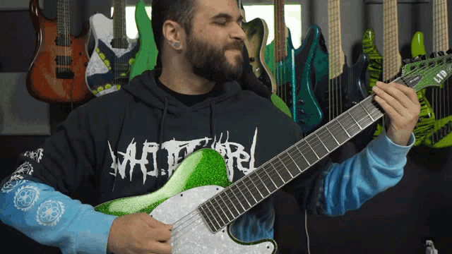 a man playing a guitar in front of a wall of guitars and a shirt that says ' metallica ' on it