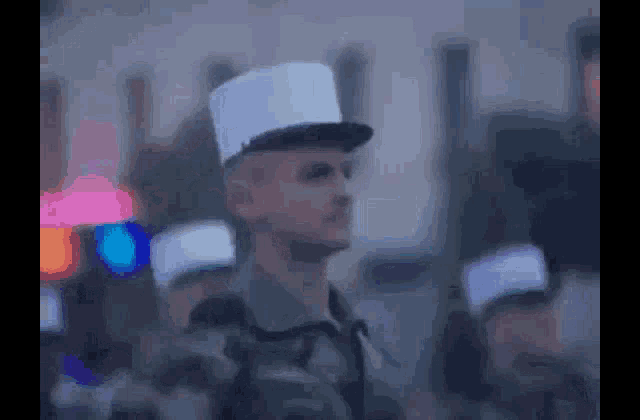 a man in a white hat is standing in a crowd of people .