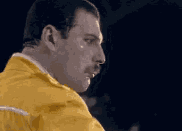 a close up of a man with a mustache wearing a yellow shirt .