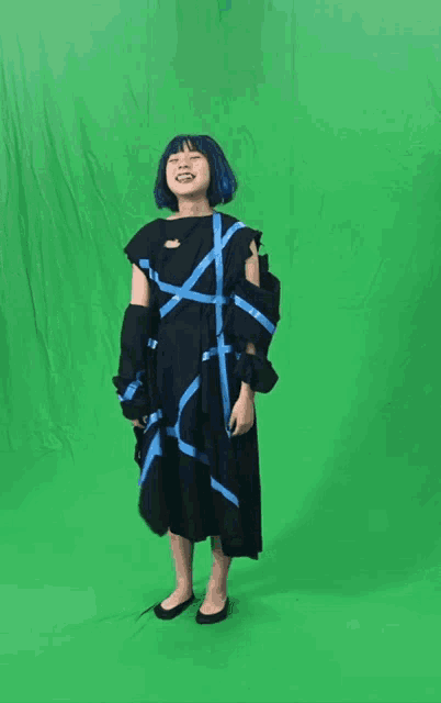 a woman with blue hair and a black dress giving a peace sign on a green screen