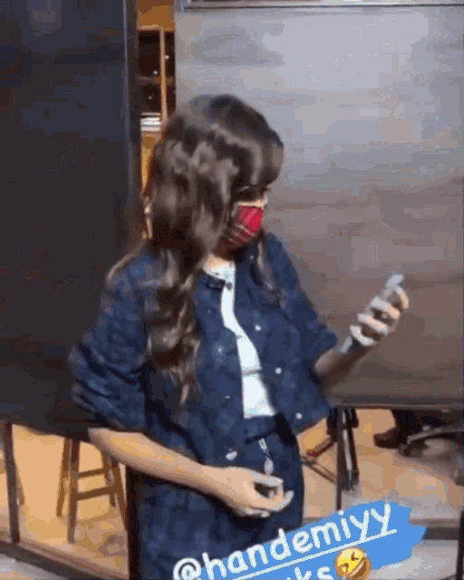 a woman wearing a mask and a denim jacket holds a bottle of hand sanitizer