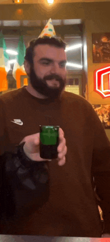 a man with a beard wearing a party hat is holding a green shot glass .
