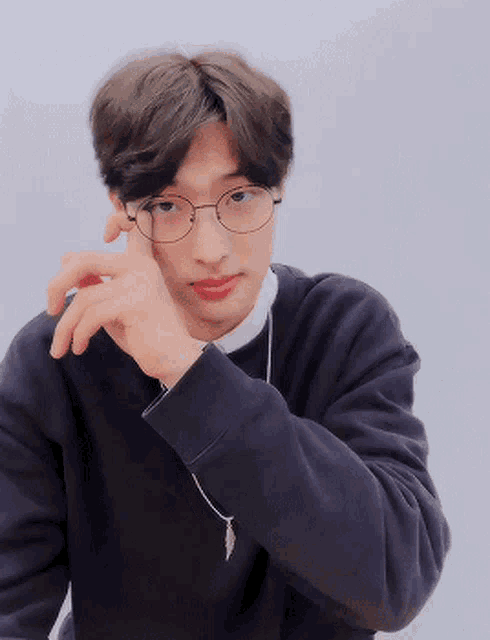 a young man wearing glasses and a black sweater is looking at the camera .