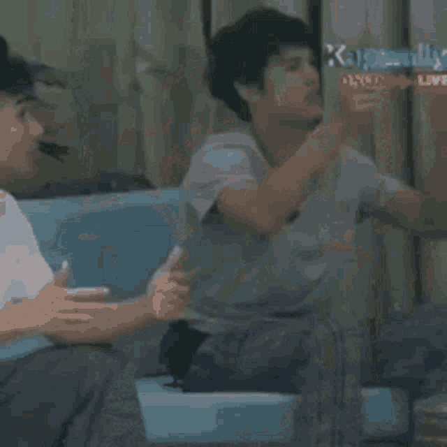 a man is sitting on a couch talking to another man while another man looks on .