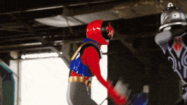 a red and blue superhero is fighting a black superhero