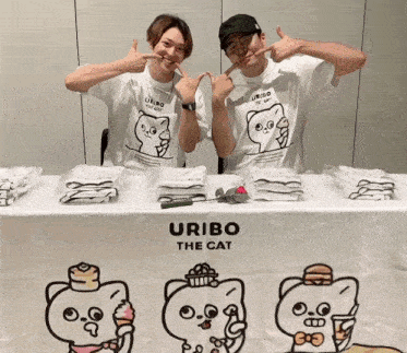 two men are standing in front of a table with uribo the cat t-shirts on it