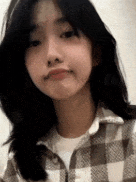 a close up of a girl wearing a plaid shirt making a face .