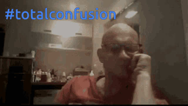 a man in a red shirt is sitting in front of a sign that says total confusion