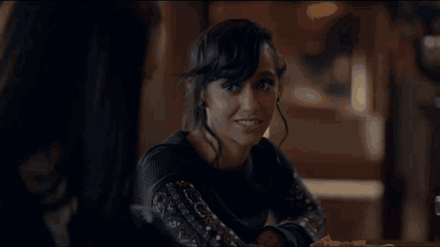 a woman in a black sweater sits at a table with a pizza