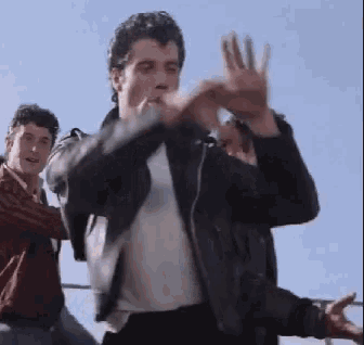 a man wearing a leather jacket is making a heart shape with his hands .
