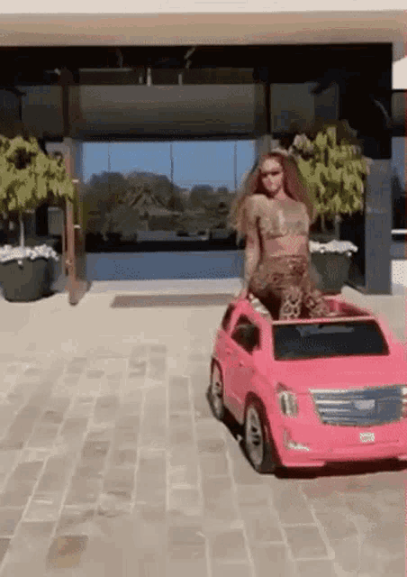 a woman is sitting on top of a pink toy car in front of a building .